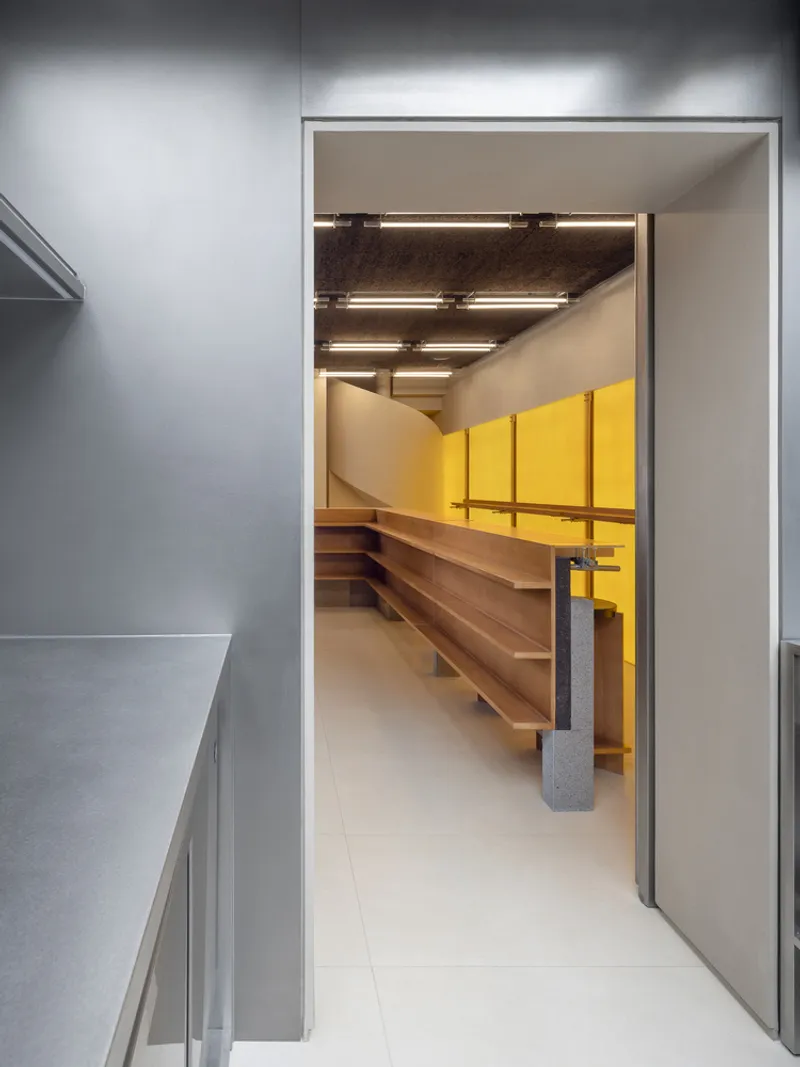 View through a doorway revealing timber shelving and yellow acoustic panels under an exposed concrete ceiling
