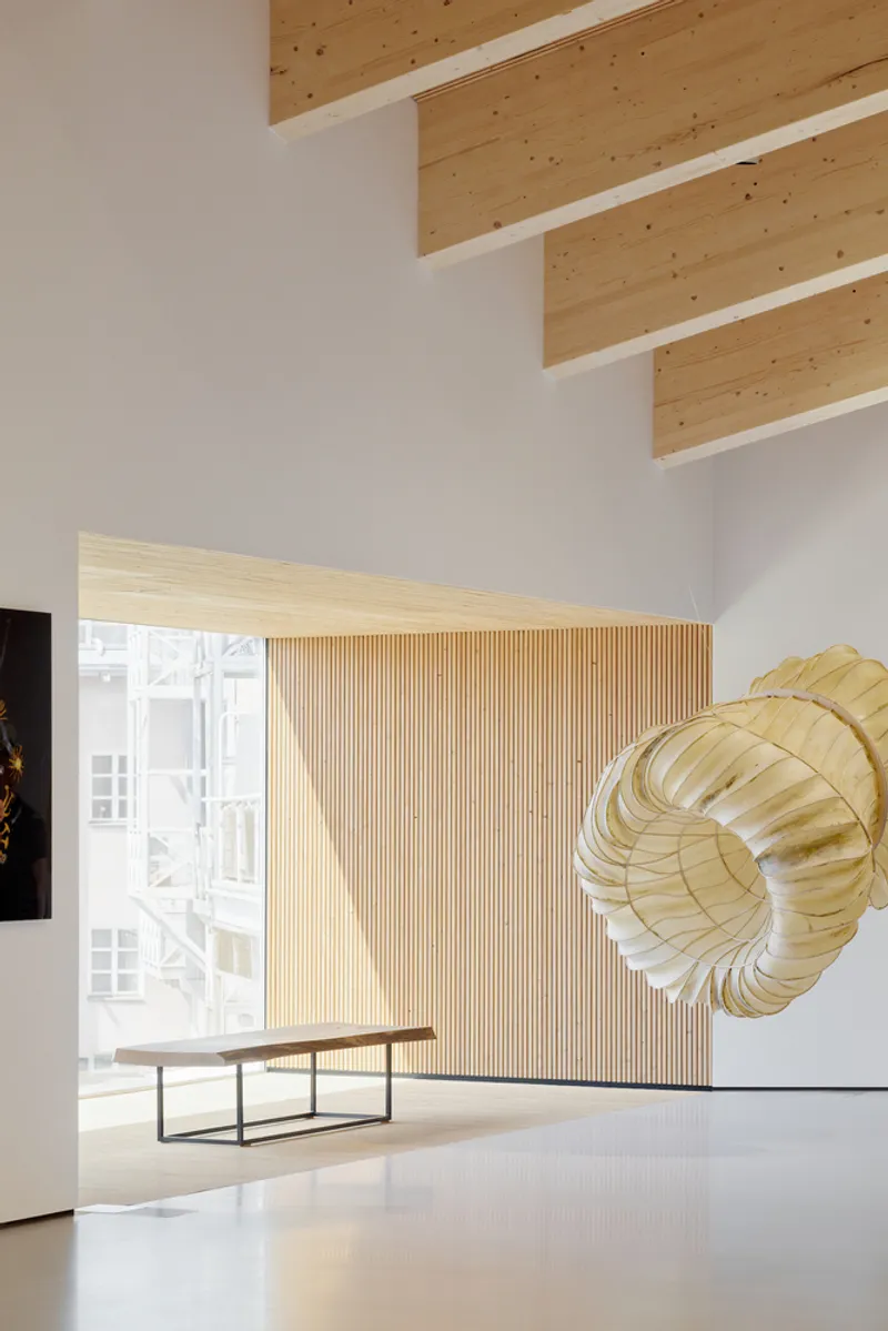 Gallery space with vertical timber slat wall beneath exposed ceiling beams and a sculptural installation
