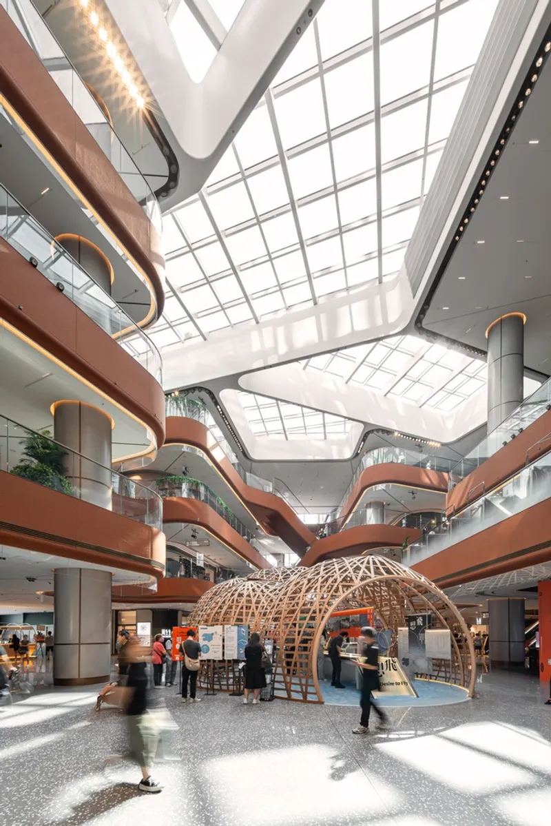 Multi-level atrium with curved terracotta balconies and a woven timber pavilion under skylights