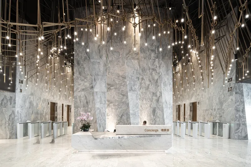 Lobby reception desk with veined marble walls and cascading pendant lights suspended from the ceiling