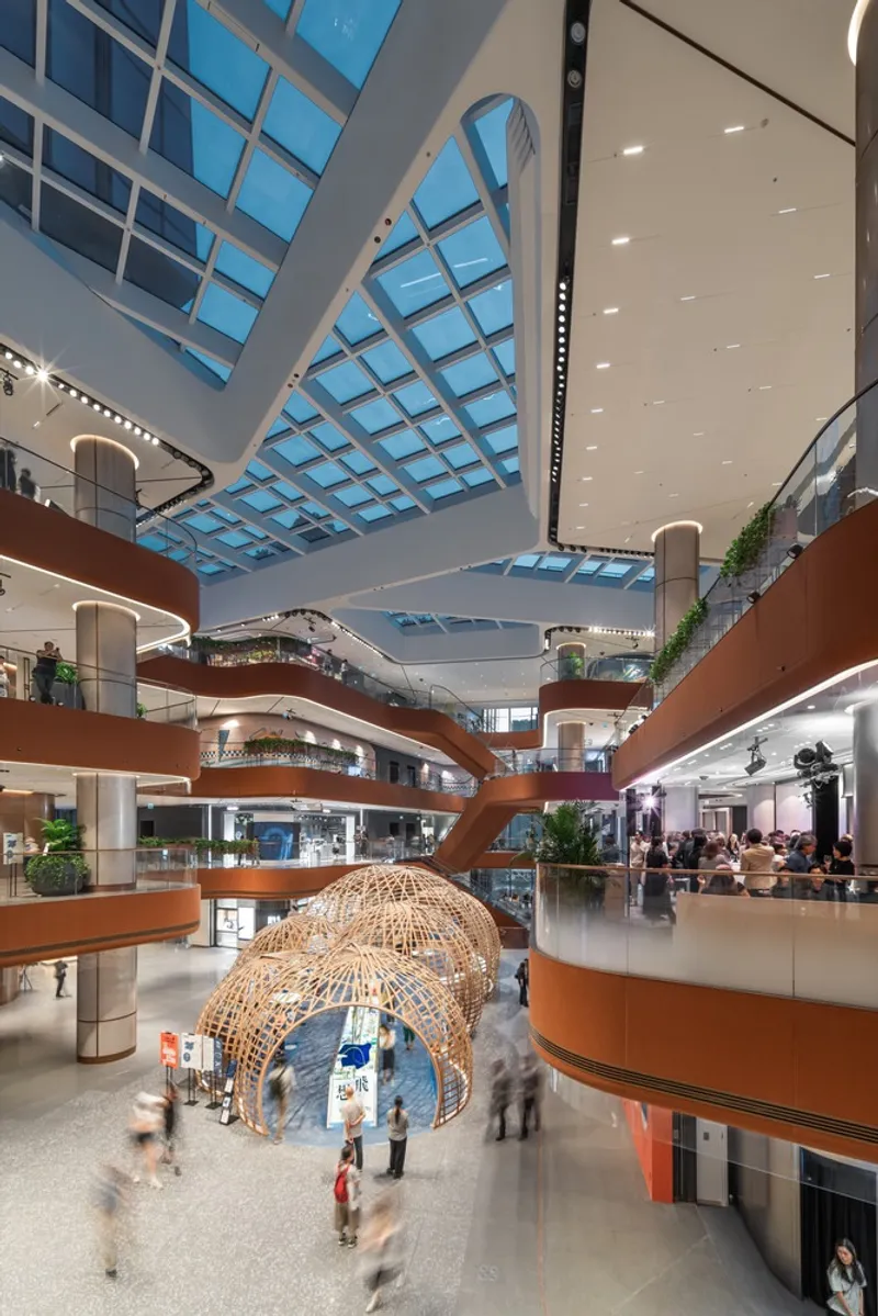 Multi-story atrium with curved bronze balconies and a woven bamboo pavilion structure surrounded by blurred visitors