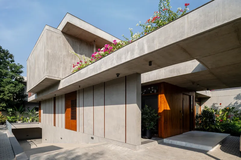 Entrance facade with cantilevered concrete slabs, timber shutters, and flowering plants on the roof terrace