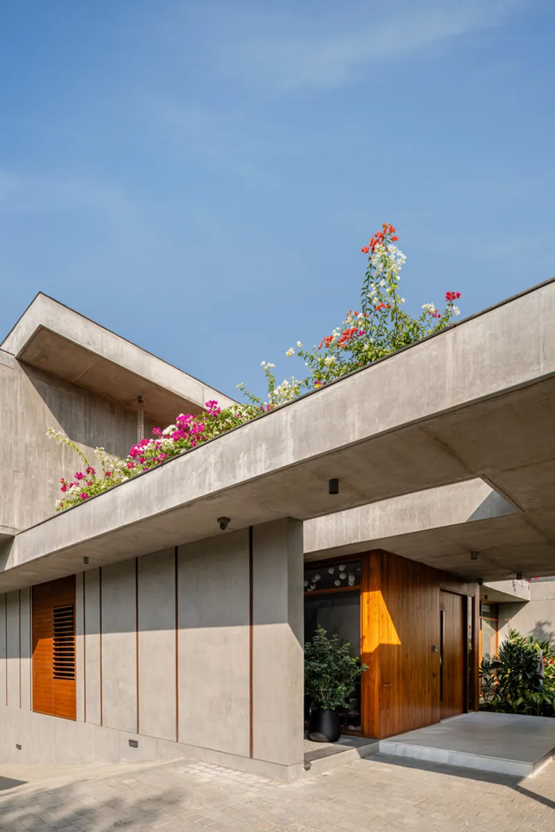 Cantilevered concrete entrance canopy with flowering bougainvillea spilling from the upper terrace against blue sky