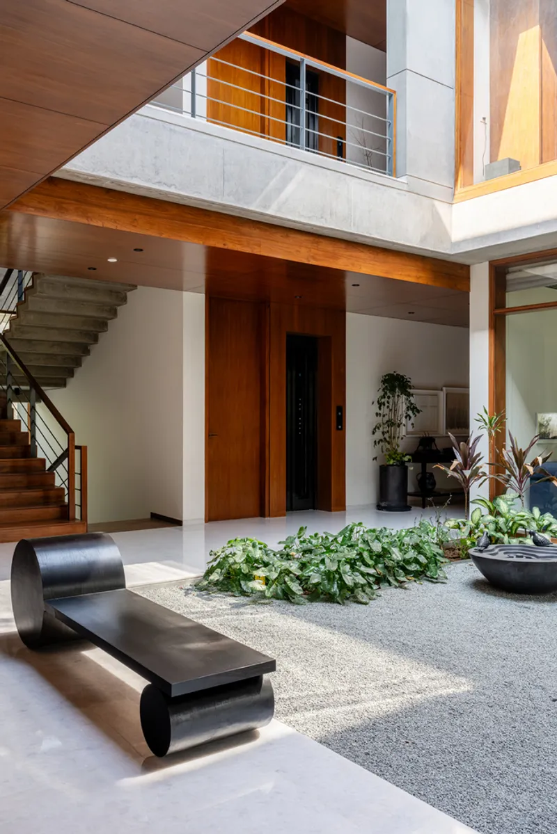 View across courtyard showing timber staircase, upper-level balcony railing, and planted bed below