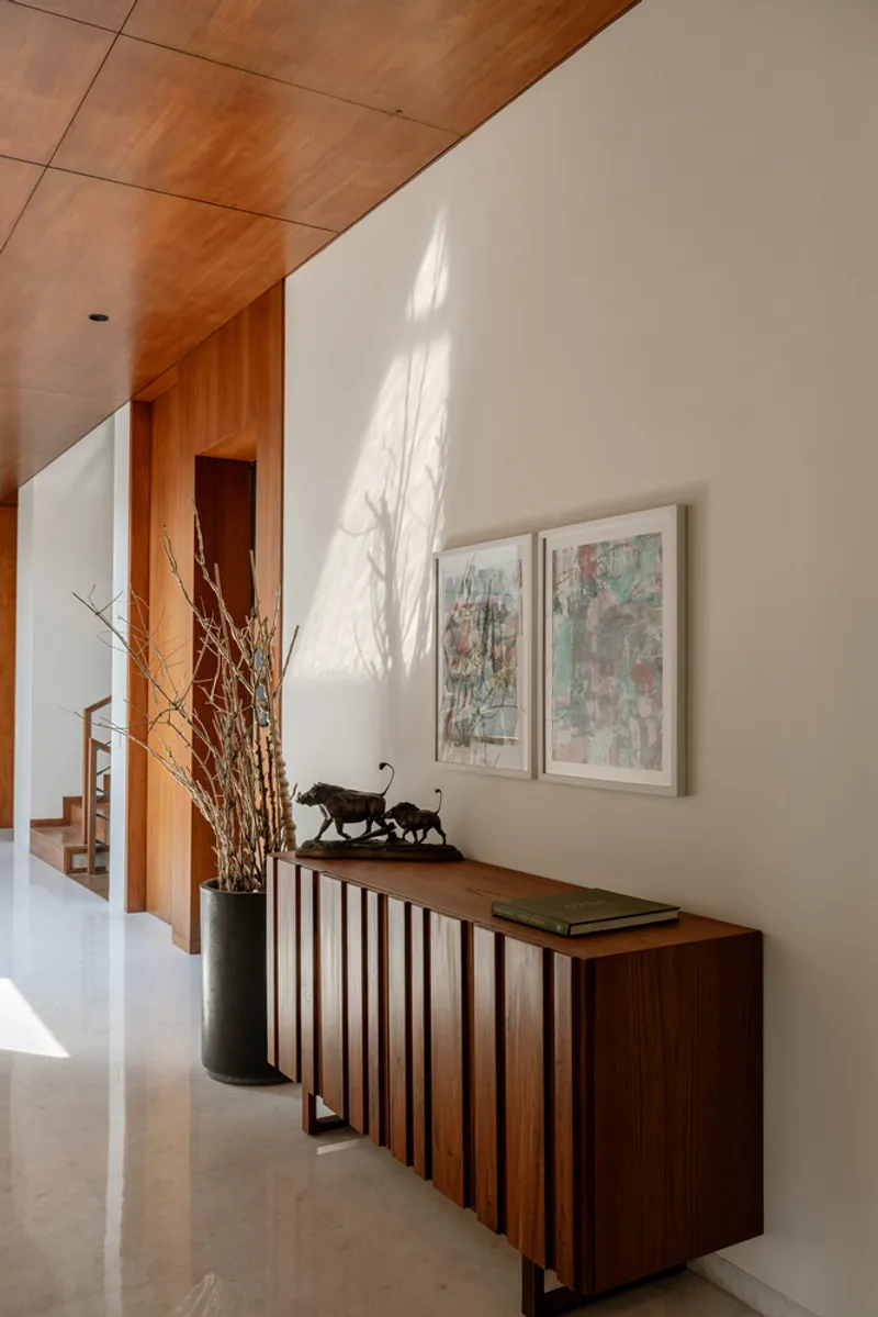Hallway with timber-slatted credenza and angled wood ceiling panel casting shadow patterns on white walls