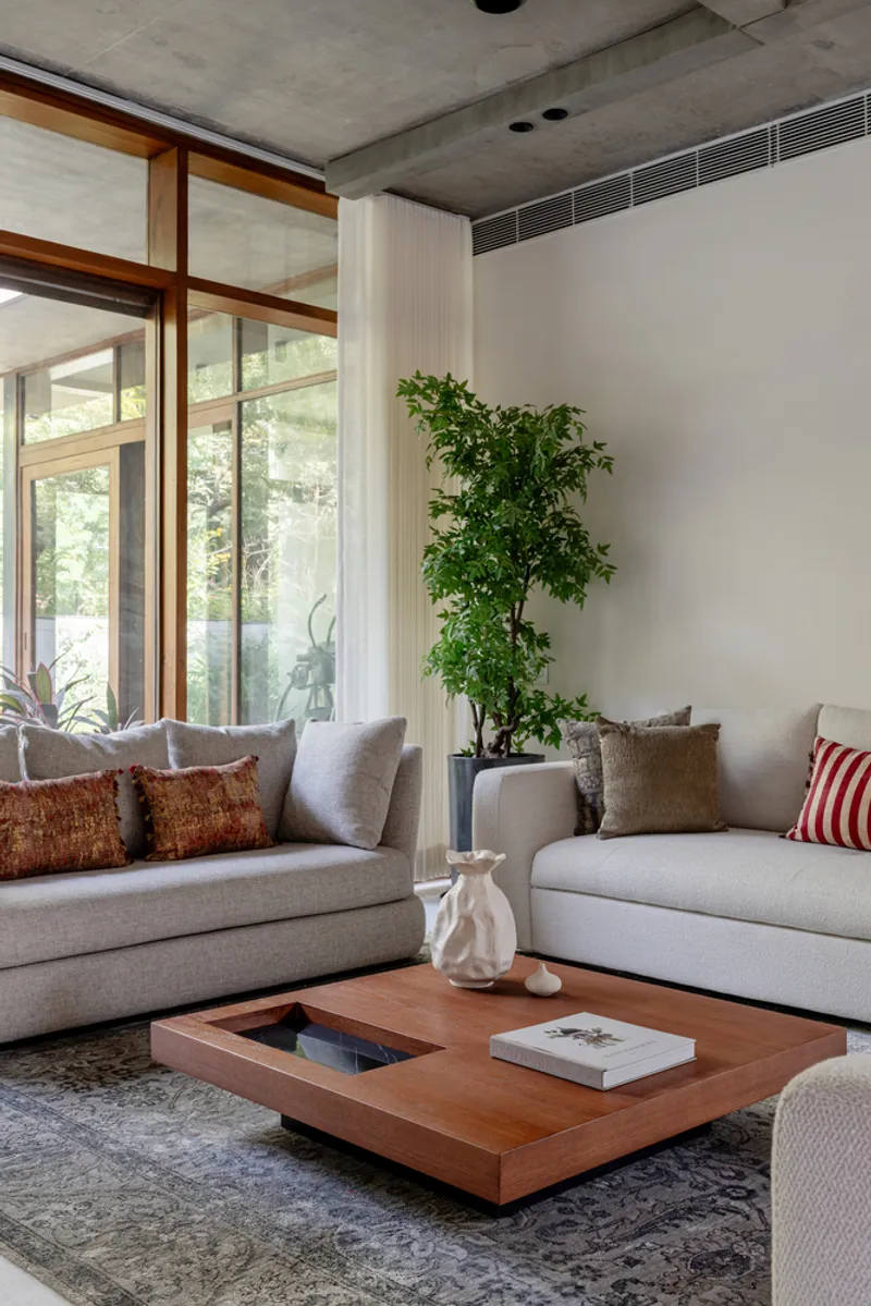 Living room with exposed concrete ceiling and floor-to-ceiling timber-framed windows overlooking greenery