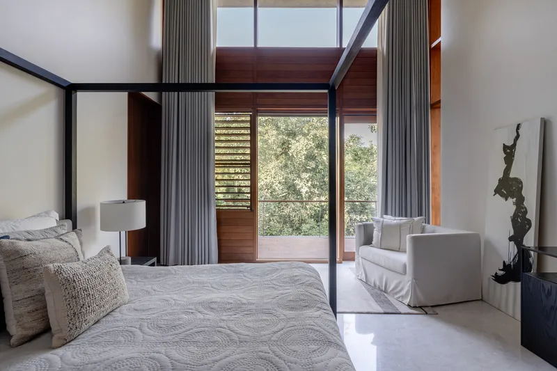 Bedroom with black steel canopy bed frame and glazed doors opening to a balcony with trees