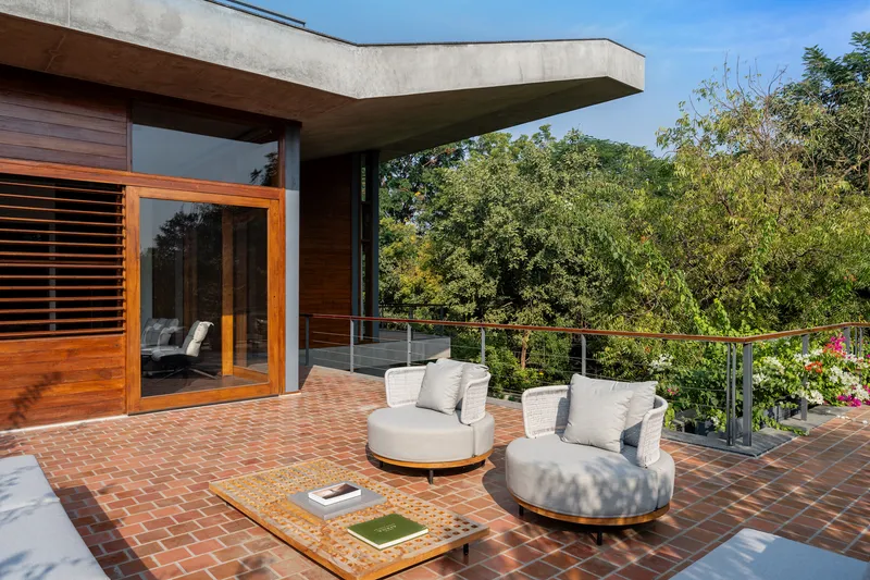 Brick-paved terrace with curved seating beneath a cantilevered concrete overhang and cable railing