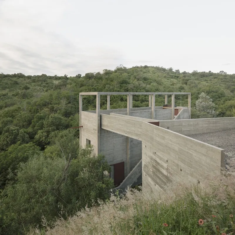 Cantilevered concrete volumes with open terrace framed by columns overlooking forested valley under overcast sky