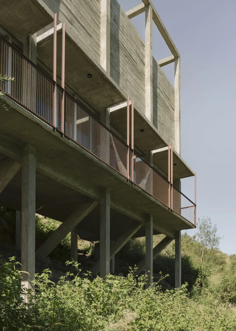 Underside view of elevated concrete structure with metal mesh balcony railings supported by angled pilotis