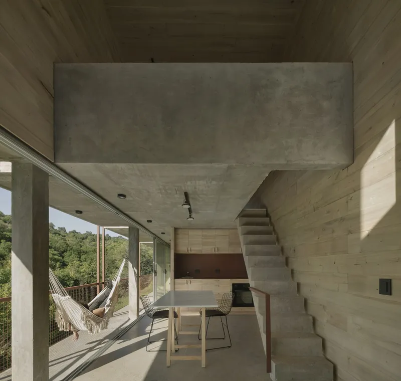 Interior living space with board-formed concrete walls, diagonal stair and hammock catching afternoon sunlight