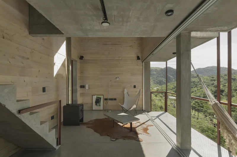 Interior living space with exposed concrete ceiling, timber wall panels, and sliding glass doors overlooking forested hillsides