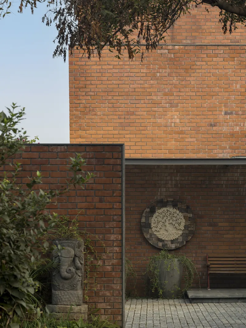 Layered brick facade with stone sculpture and tree branches overhead at dusk