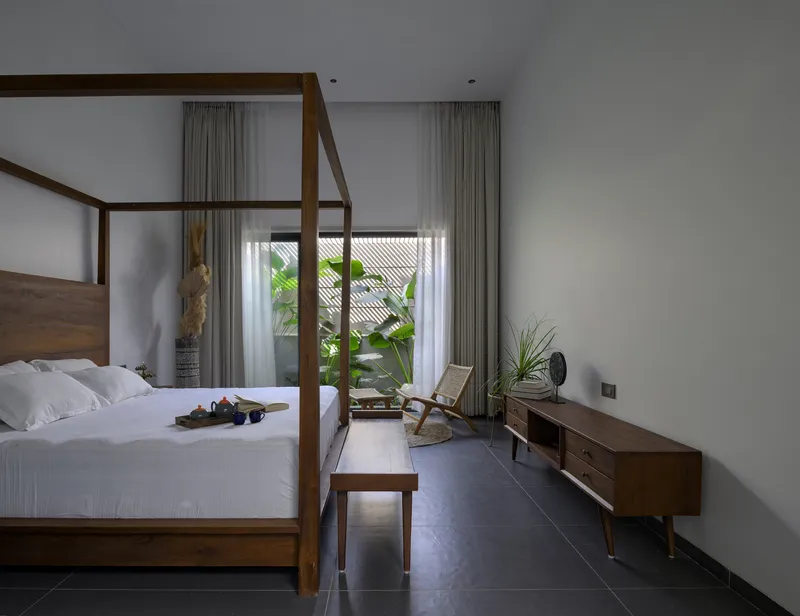 Bedroom with timber four-poster bed and sheer curtains framing view to planted courtyard