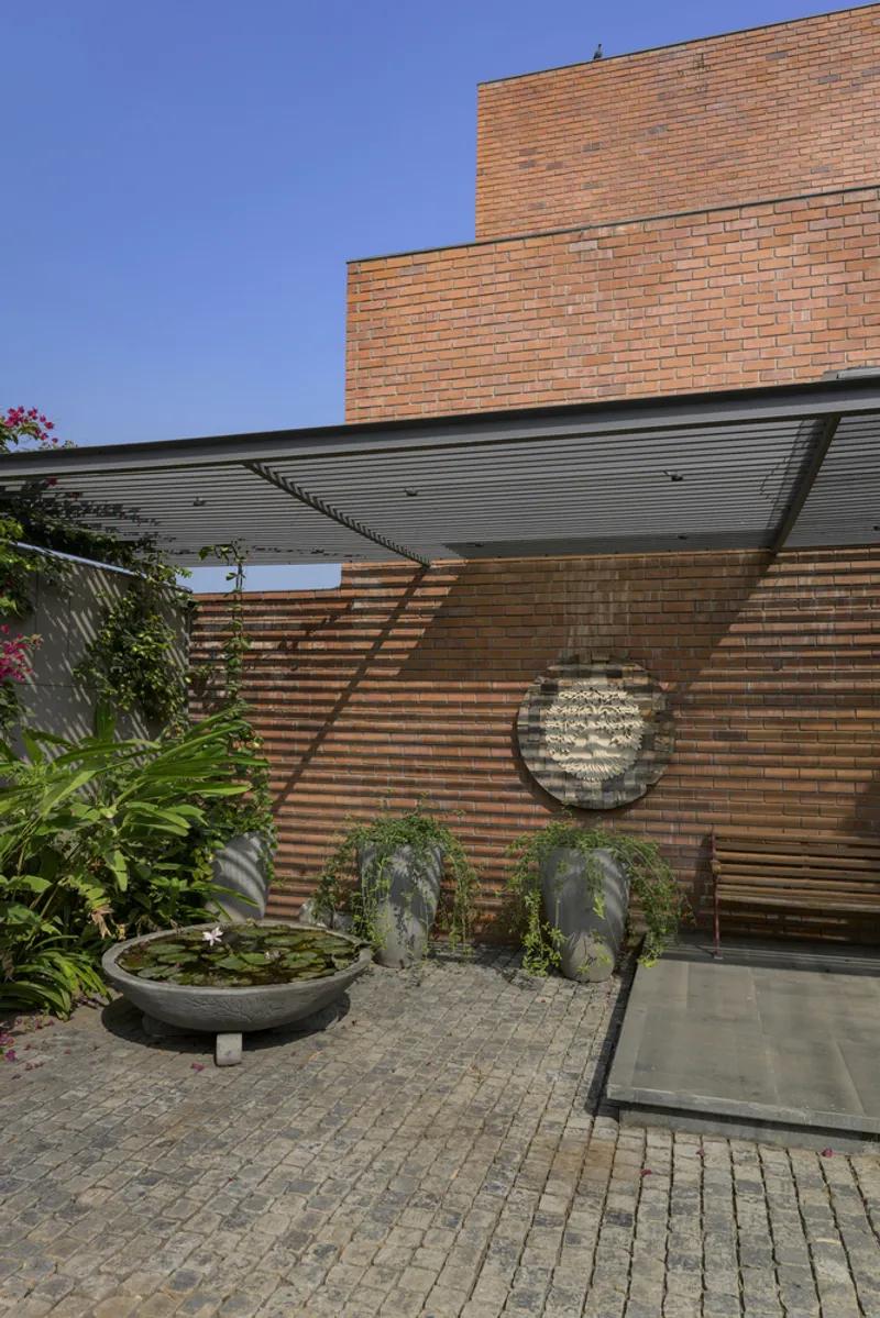 Entry courtyard showing circular sculptural relief on brick wall beneath slatted wood screen and canopy