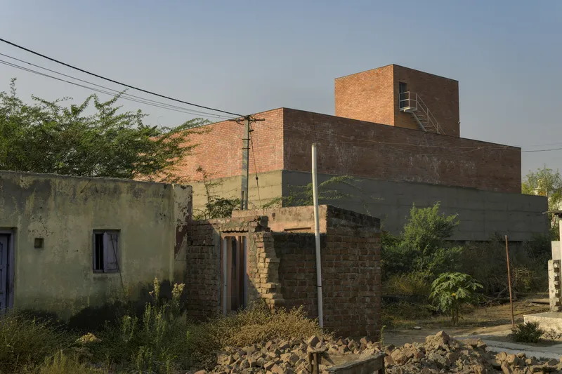 Red brick tower and volumes behind weathered low-rise structures and power lines at dusk