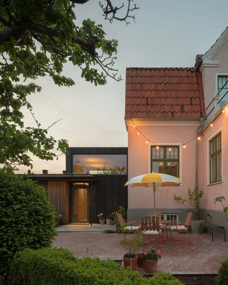 Brick patio with outdoor furniture and string lights between the dark annex and red tile roof at dusk