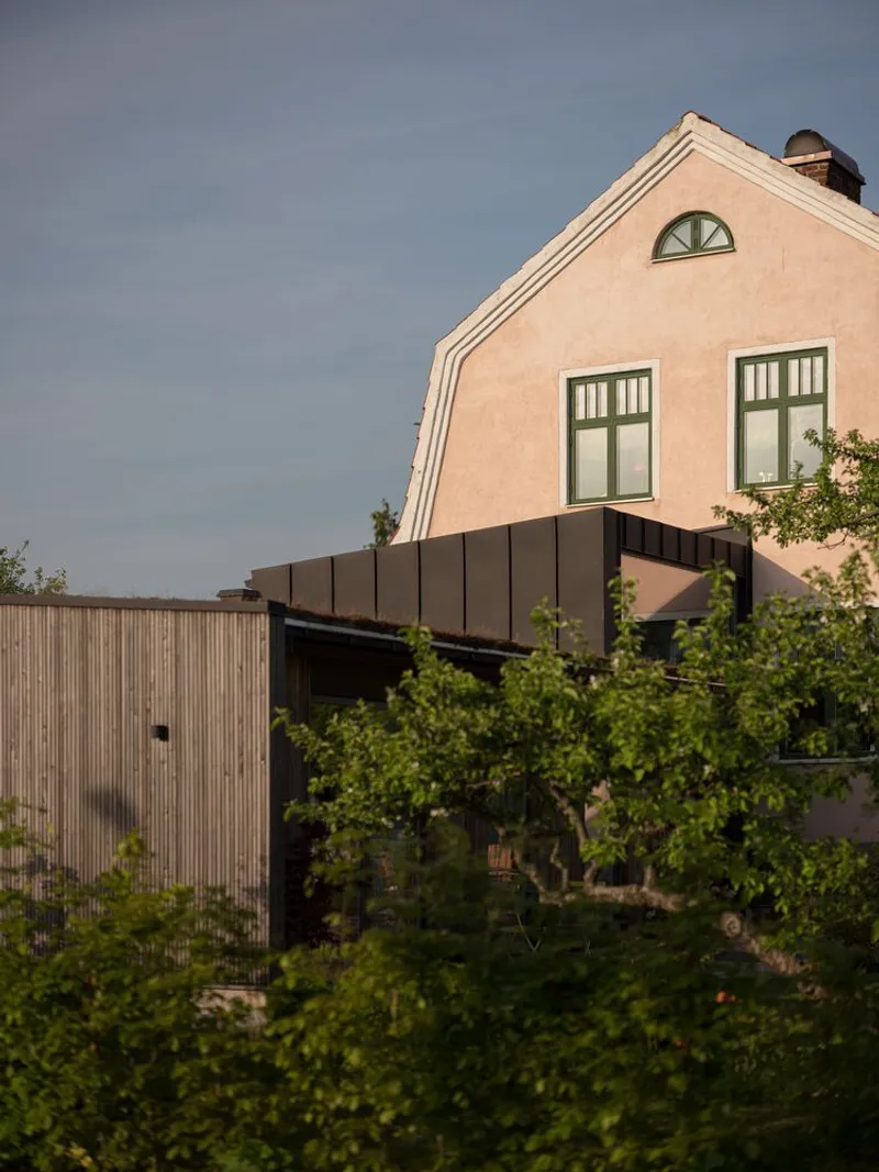 Evening view of the timber-clad addition with dark metal parapet beneath the arched window of the existing gable