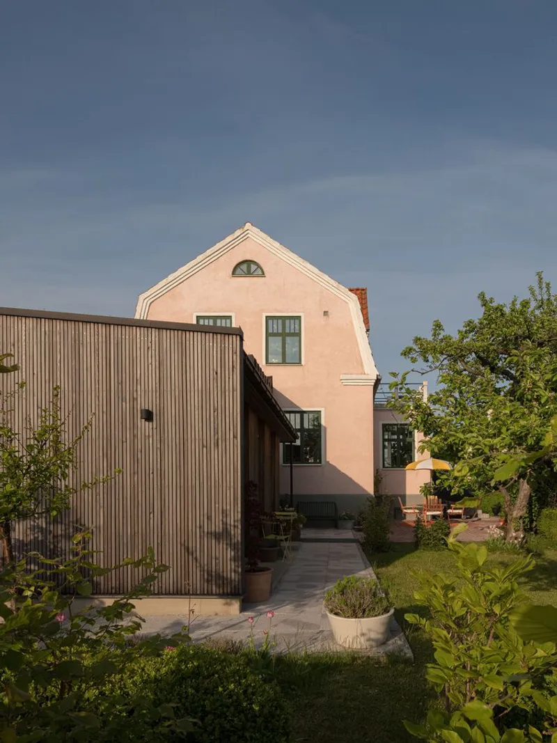 Garden facade showing the vertical timber extension connecting to the peach rendered house in late afternoon light