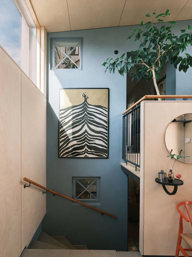 Stairwell with blue-painted wall displaying zebra artwork and indoor tree beside plywood balustrade and metal railing