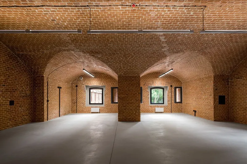 Vaulted brick interior with central column and arched window openings filtering natural light