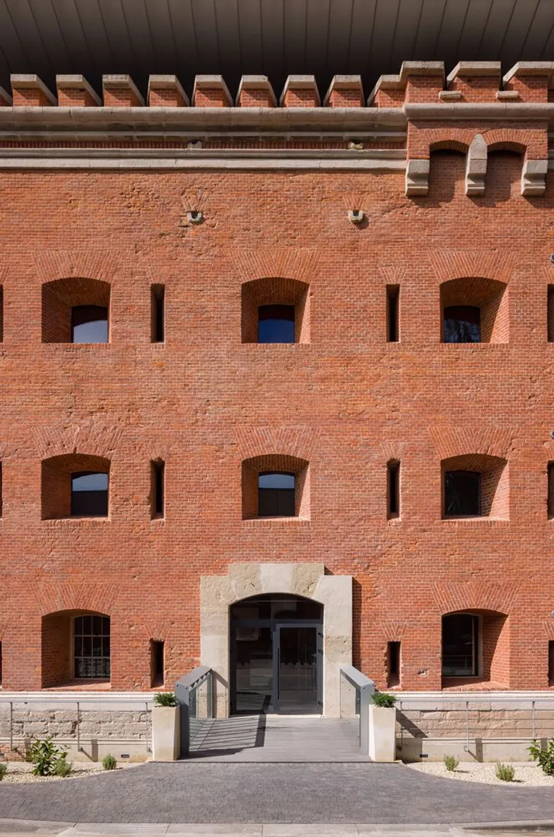 Red brick facade with arched window openings and crenellated parapet beneath an overcast sky