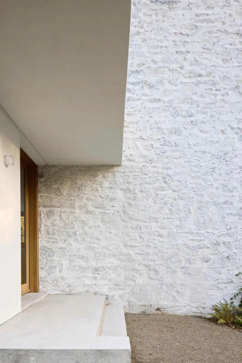 Junction of painted render soffit and whitewashed stone wall at entrance with timber door visible