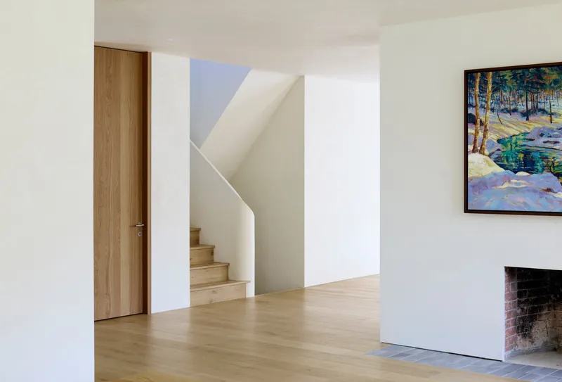 Interior hallway with oak flooring showing timber staircase through angled opening beside exposed brick fireplace