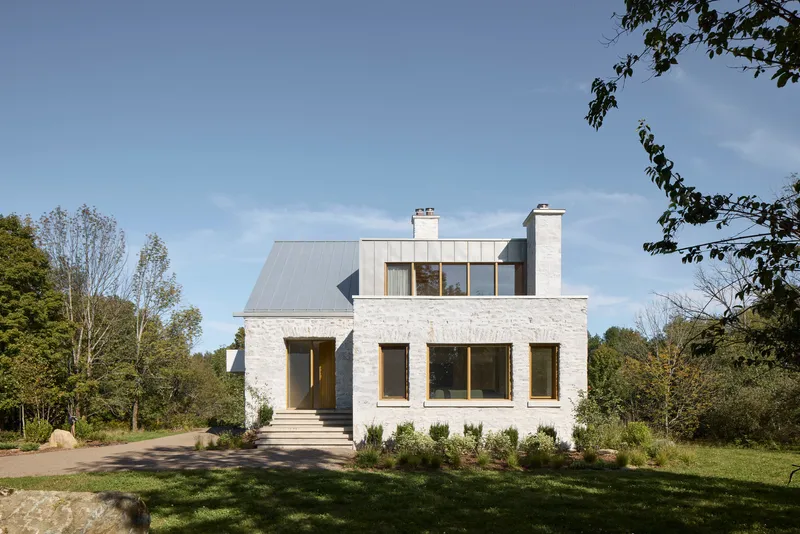 Front facade of whitewashed brick residence with timber framed windows and standing seam metal roof