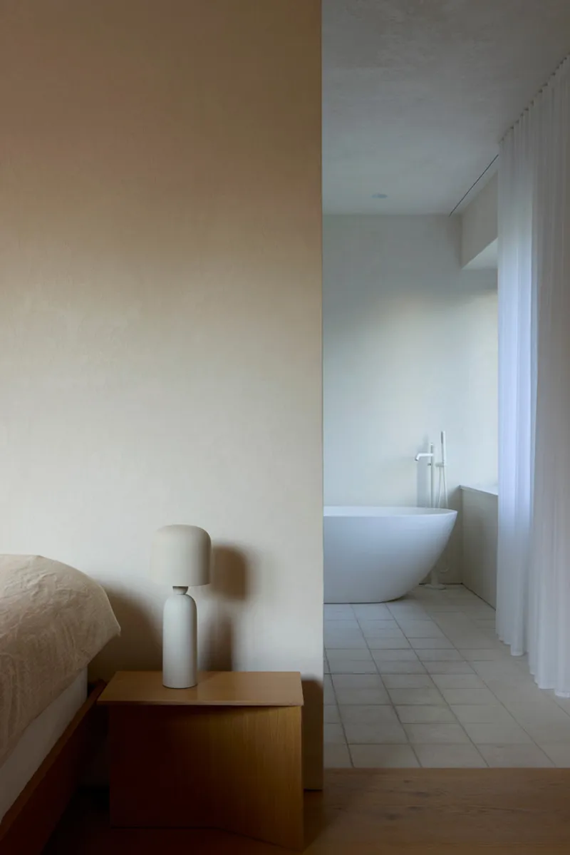 View from bedroom through doorway to ensuite bathroom with freestanding tub and white sheer curtain