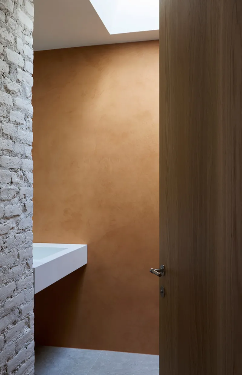 Hallway with ochre plaster wall, white brick wall, timber door and overhead skylight
