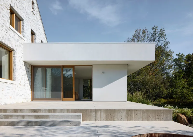 White stucco addition with sliding glass doors and concrete steps beside white-painted brick gable