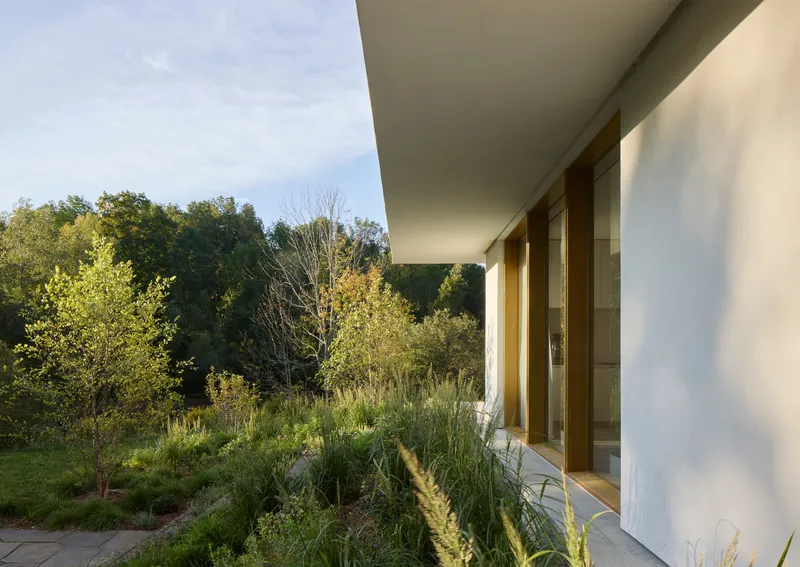 Covered terrace overlooking planted meadow with grasses and trees in late afternoon light