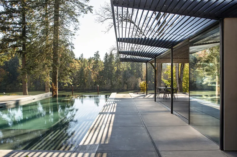 Covered terrace with steel louvered canopy casting shadows onto concrete paving beside a reflecting pool