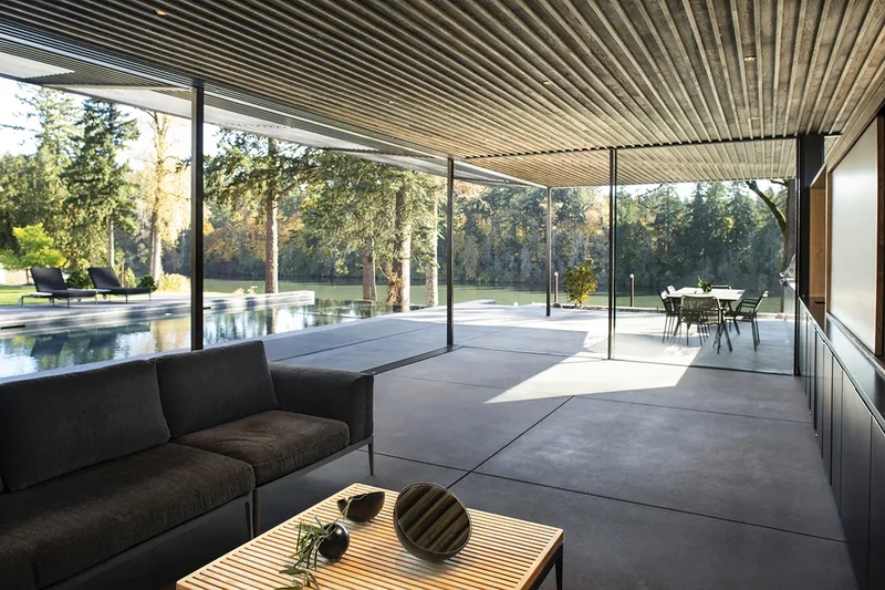 Glass-enclosed living area with slatted wood ceiling opening to pool terrace and lawn beyond