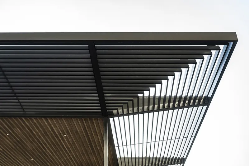 Corner detail of the steel-framed louvered roof canopy against an overcast sky