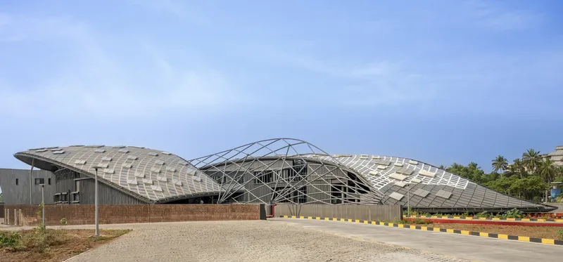 Long view of the undulating shell roof with steel structure above brick perimeter walls under clear sky