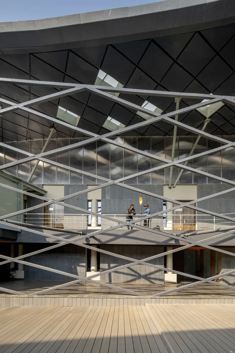 Diagonal white steel bracing across the facade with timber deck and two people on an interior balcony