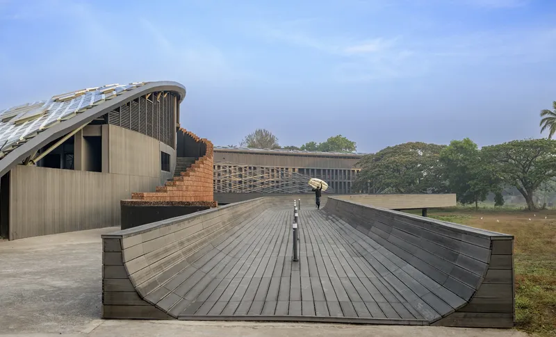 Curved timber deck amphitheater with person holding umbrella descending toward trees and overcast horizon