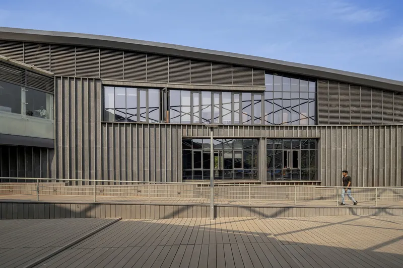 Timber deck plaza fronting a vertical louver facade with geometric screen panels above glazing