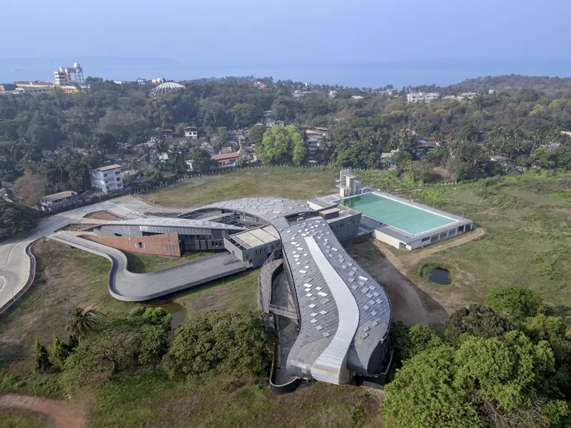 Aerial view of the looping roof form and surrounding buildings nestled in green hillside terrain