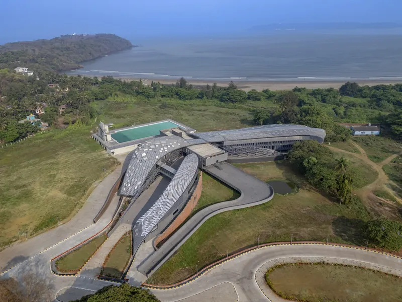 Aerial view of curved metal-clad volumes surrounding courtyard with coastal landscape beyond