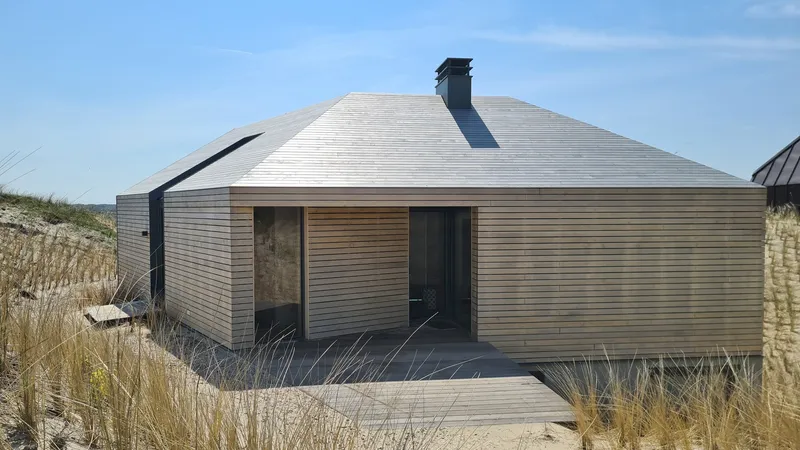 Front facade showing horizontal timber cladding and grey panels beneath a sloped metal roof under clear skies
