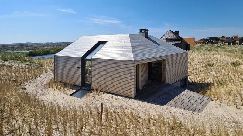 Elevated view of the horizontally-clad timber and grey-paneled volumes nestled in sandy dunes with beach grasses