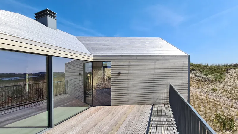Rooftop terrace with timber decking and metal grating connecting grey-clad and timber-clad volumes under blue sky