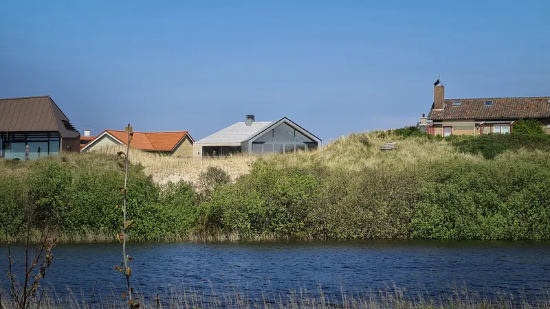 Distant view across the pond showing the gabled roof among neighboring houses and dune vegetation at dusk