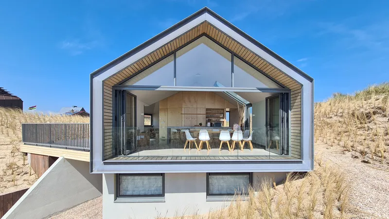 Fully glazed gable end opening onto dining area with timber ceiling and dune grasses flanking