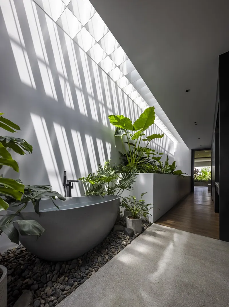 Interior corridor with freestanding bathtub surrounded by planted beds beneath a slatted skylight casting diagonal shadows
