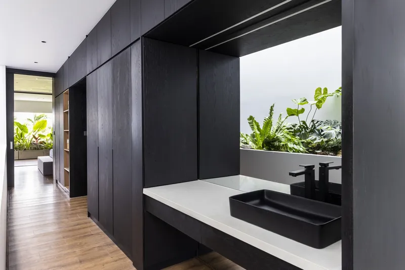 Bathroom vanity with black sink and fixtures set against dark timber cabinetry looking toward planted courtyard