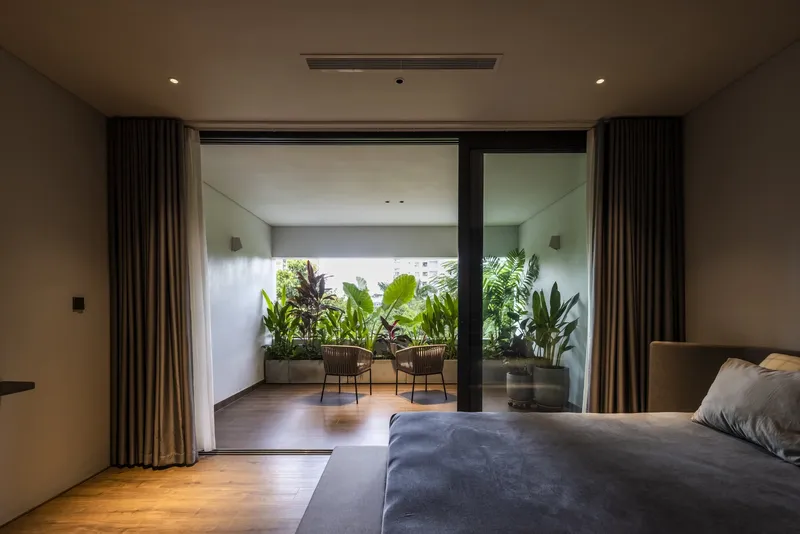 Bedroom with glazed doors opening to a timber deck with planted beds under overcast sky
